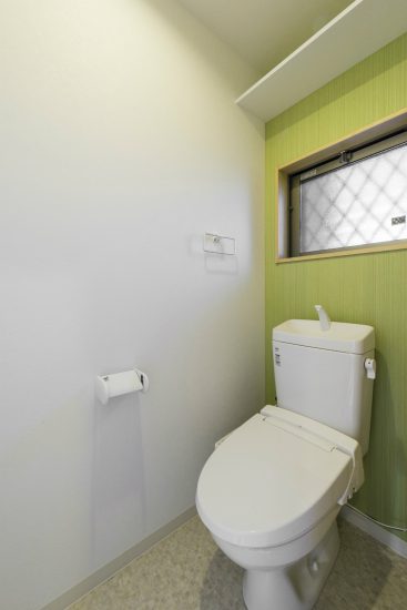 愛知県日進市のメゾネット賃貸の緑色のアクセントクロスがおしゃれな窓付きのトイレ