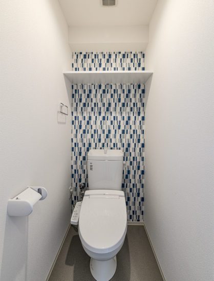 愛知県豊田市の12階建ての賃貸マンションの収納棚付きのモダンなアクセントクロスのあるトイレ