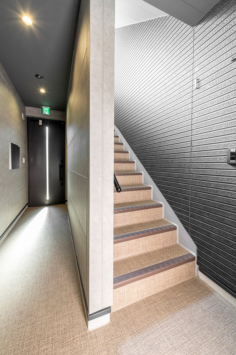 名古屋市北区の約60坪の土地の木造3階建てアパートのモダンな配色とダウンライトの光が調和するエントランスホールと内階段