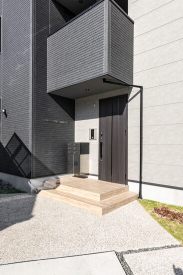 名古屋市北区の約60坪の土地の木造3階建てアパートの木目調のステップが目を引く宅配ボックスを完備したモダンなエントランスポーチ